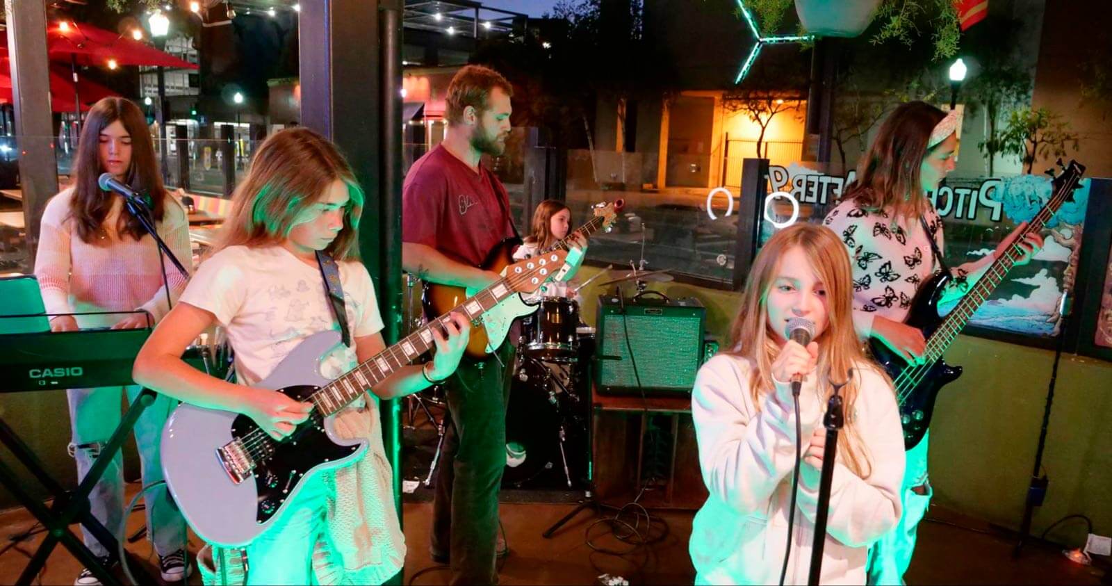 User-Inserted A group of young musicians performs on stage, featuring guitars, keyboards, and drums, with colorful lights creating a lively atmosphere.